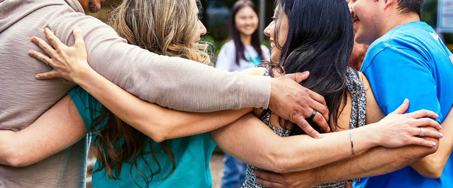 Group of people in a close embrace demonstrating strong community bond during a gathering, possibly supporting the local programs.