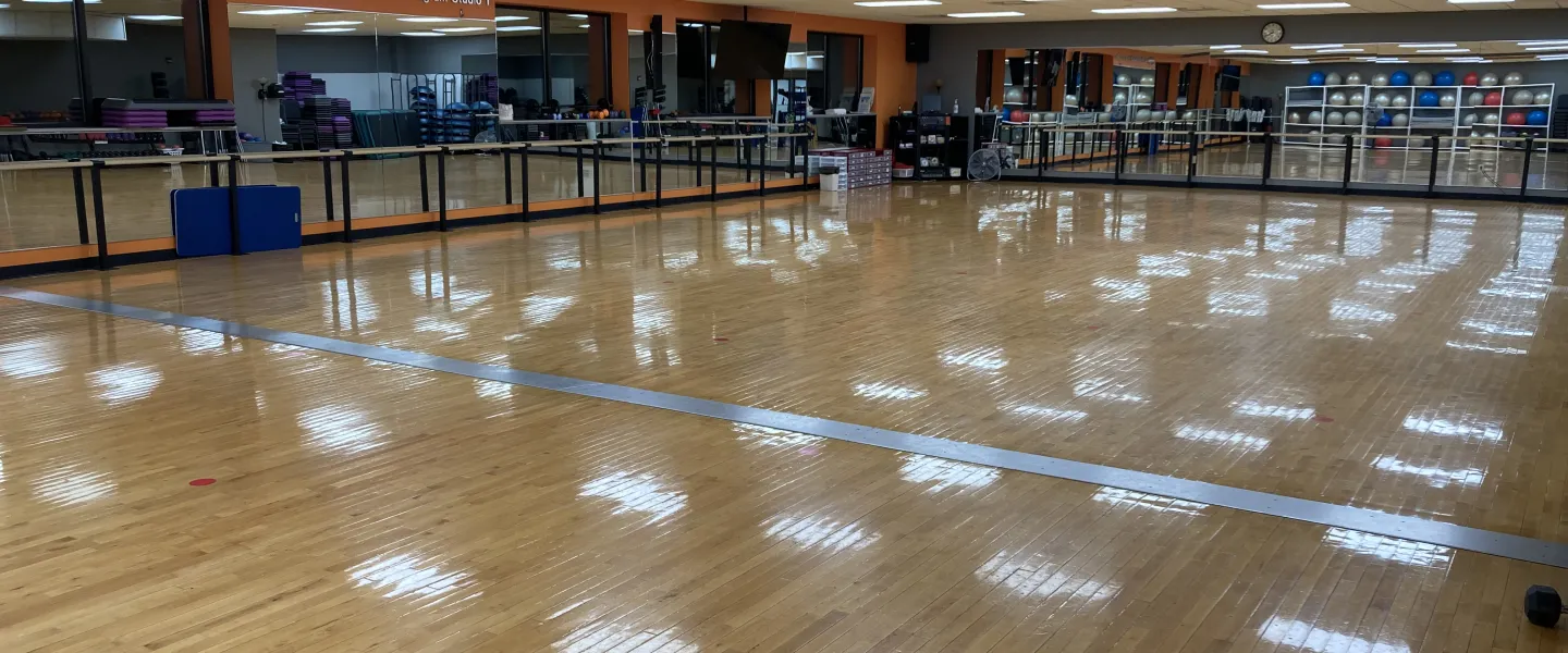 Empty fitness studio with a wooden floor and exercise equipment; a space for community activities and kids' programs.
